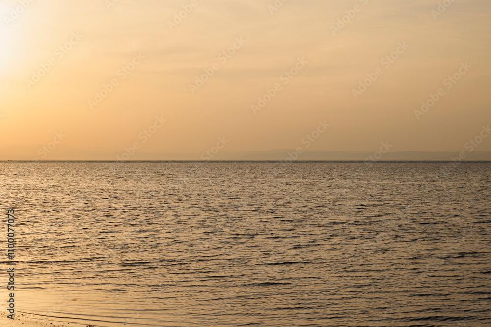 Obraz premium alba sul mare calmo, lungo la costa vicino alla città di Grado, nell'Italia nord orientale, con vista fino all'orizzonte, con un cielo coperto dalla foschia