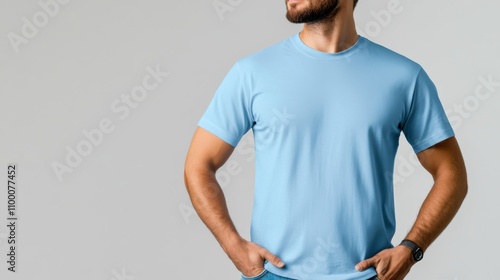 A casual man stands with his hands in his pockets, wearing a blue t-shirt, projecting a calm and confident demeanor, against a plain background setting. photo