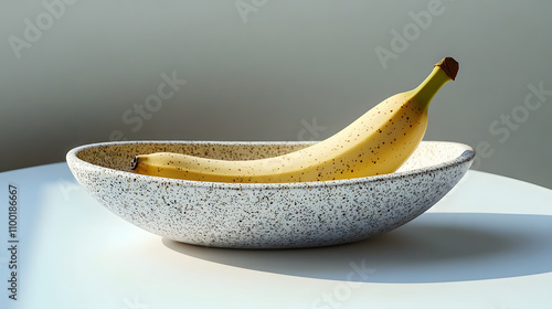 A single ripe yellow banana in a speckled oval bowl on a white table.