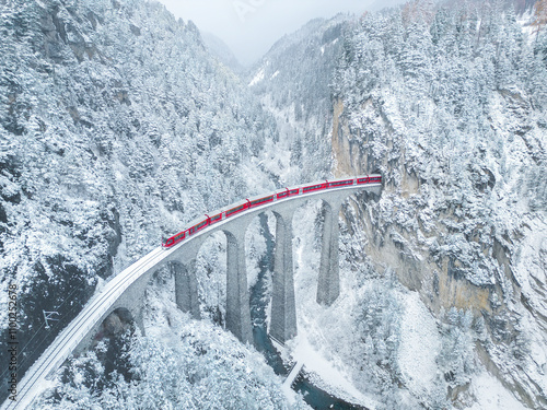 Aerial view of landwasser viaduct with a red train crossing over snowy mountains, Bergun Filisur, Switzerland.