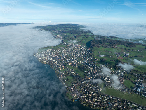 Aerial view of tranquil Uerikon village by the serene lake with misty clouds and green fields, Zurich, Switzerland. photo