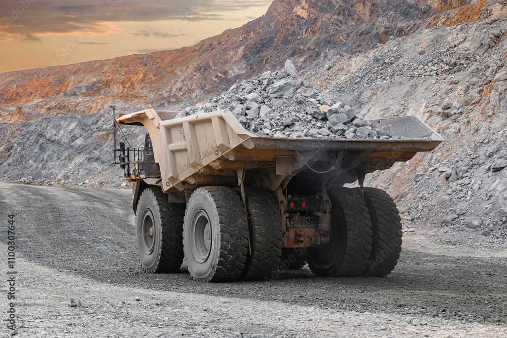 Obraz premium Massive Mining Dump Truck Transporting Rocks in Open-Pit Mine at Sunset