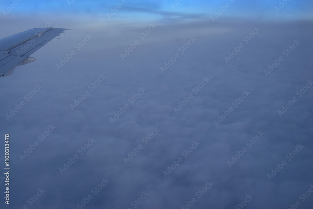 Fototapeta premium Thick layer of clouds under the wing of a flying airplane, winter vacation, airplane wing above the clouds.