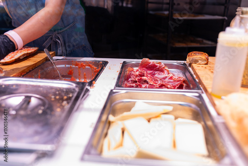 Unrecognizable butcher preparing a sandwich with serrano ham, tomato and cheese in the kitchen of a deli