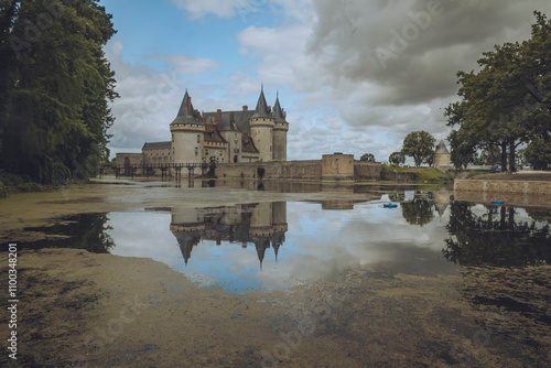 View of chateau de Sully sur Loire with reflection in the moat surrounded by trees and cloudy sky, Sully-sur-Loire, France. photo