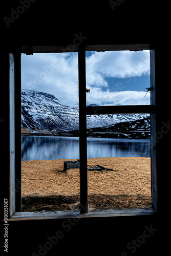 View of an abandoned shed by a serene lake with snow-capped mountains under a blue sky, Sudavik, Iceland. photo