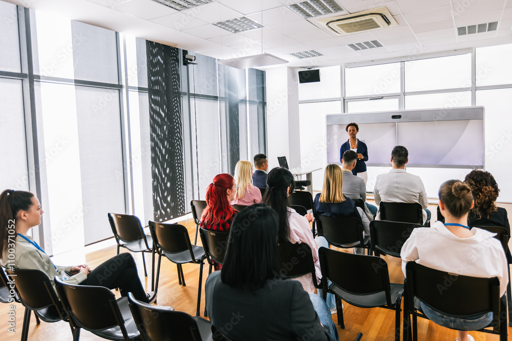 Obraz premium African American woman CEO standing in front of a multiracial group of colleagues. Multimedia classroom with smart board and graphics on them.