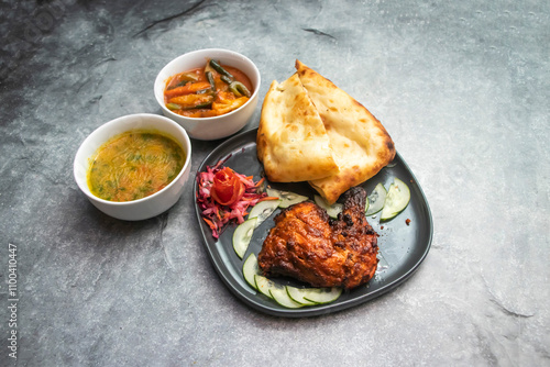 tandoori chicken leg, nan, miixed vegetables, daal, and salad served in plate and bowls isolated on grey background side view of indian, pakistani and bangladeshi food photo