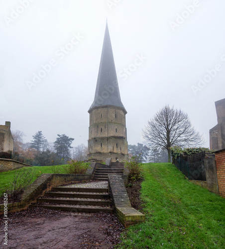 Bild auf Leinwand The pointed ancient tower of the Abbey of Saint Vinoc on a cloudy, foggy, winter day
