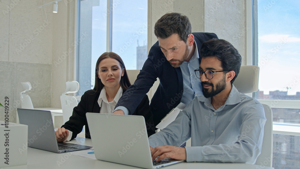Obraz premium Male CEO boss leader man businessman help office coworkers with computer work check online project on laptop talking to diverse multiracial business team colleagues brainstorm analyze sales paperwork