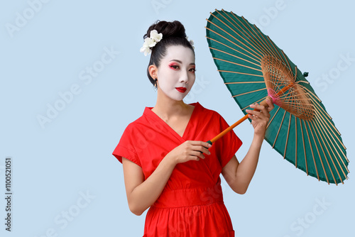 Beautiful young geisha with parasol on light background photo