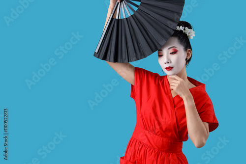 Beautiful young geisha with fan on blue background photo