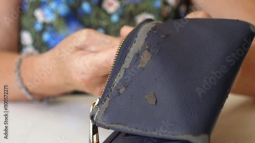 A woman's hands hold an old, worn-out wallet on a white table, showing signs of use and deciding it’s time to discard it. photo