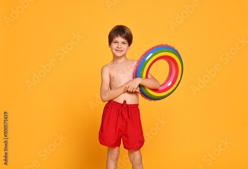 Happy little boy in beachwear with inflatable ring on orange background photo