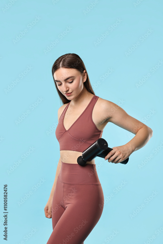 Obraz premium Woman using percussive massager to relieve abdominal muscles on light blue background