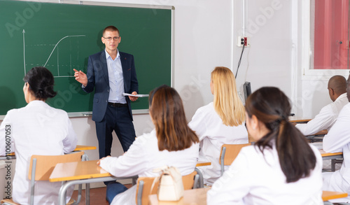 Professor of mathematics lecturing to adult students in auditorium, explaining function graph on blackboard photo