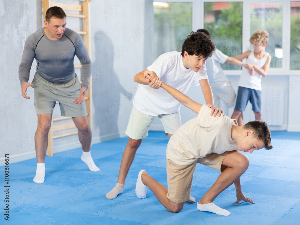 Fototapeta premium Sedulous underage practitioner of self-defense courses applying arm twist on his opponent in standing position