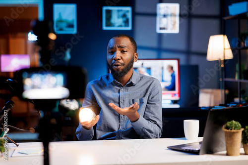 BIPOC media star discussing video subject related to home enhancement. Internet show host presenting dimmable smart light bulb able to change colors to viewers, demonstrating features photo