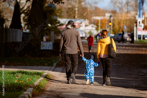 A loving couple strolls through a sunlit park with their young son, surrounded by the vibrant colors of autumn, enjoying a joyful and peaceful family moment together. photo