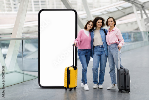 Three friends smile happily as they pose with their suitcases in a contemporary airport terminal, showcasing a stylish empty screen behind them for travel plans or marketing. photo