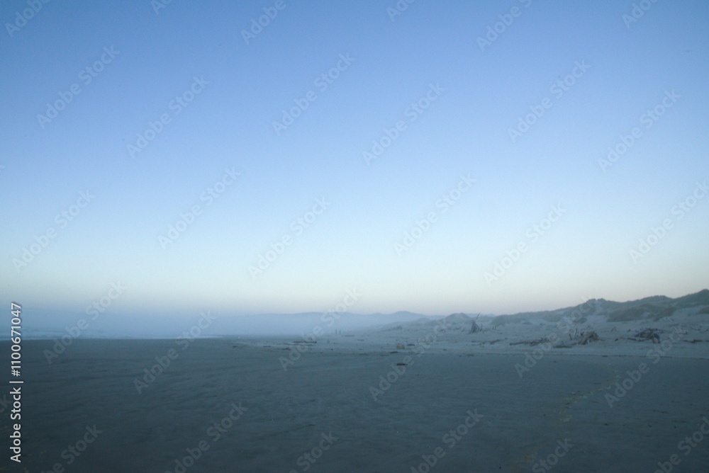 Fototapeta premium View across the beach at dusk, with blue light along the horizon over the ocean. 