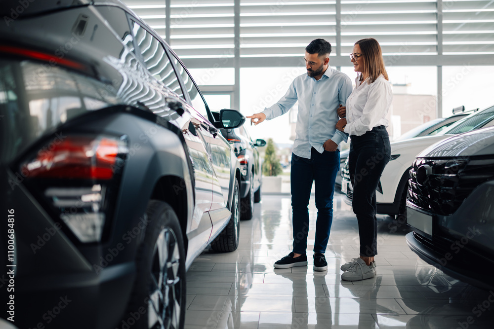 Obraz premium Couple examining the exterior of luxury car in dealership showroom