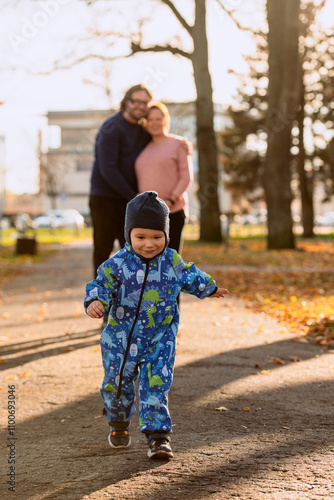 A joyful little boy in his winter coat and hat plays happily in the park, surrounded by the love and warmth of his smiling parents photo