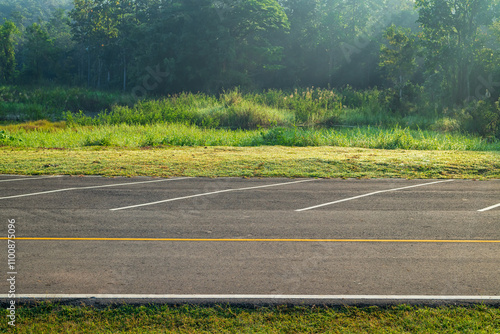 Empty parking lot against meadow and beautiful forest with light in morning.