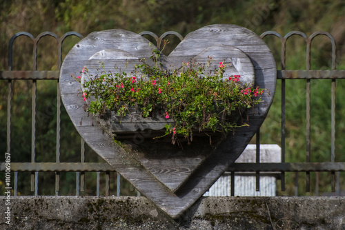 Un cuore di legno con un vaso pieno di fiori rossi su un ponte che attraversa un torrente a Forno di Zoldo nelle dolomiti bellunesi photo