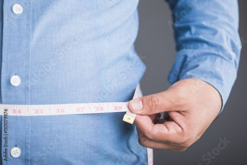 An overweight person wearing a tight shirt, using a measuring tape around their waist to track their size, symbolizing awareness and management of body weight