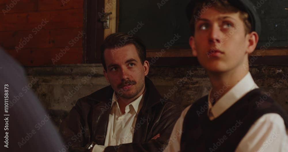 1930s 1940s concept - a group of men sits in a hideout and talk. A young man with a mustache asks a boy a question 1930s 1940s concept - a group of men sits in a hideout and talk. A young man with a mustache asks a boy a question