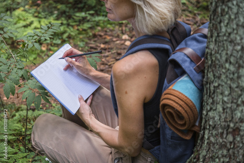 Blonde woman sitting under tree with notebook in forest