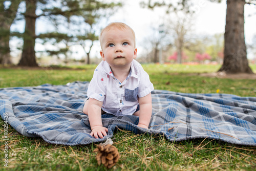 Baby boy crawls on blanket at the park between trees photo