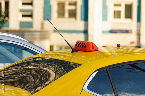 A vibrant yellow taxi waiting under the sun outside busy buildings in the city during a clear day photo