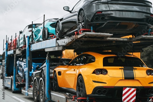 Exotic luxury sport cars with shiny performance and power are transported on a two-level hydraulic trailer truck. They are either heading to a racing championship or a car show photo