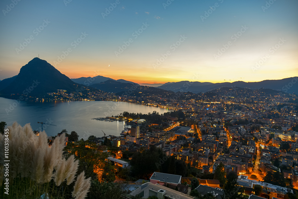 sunset over lake lugano with the lights of the city turning on