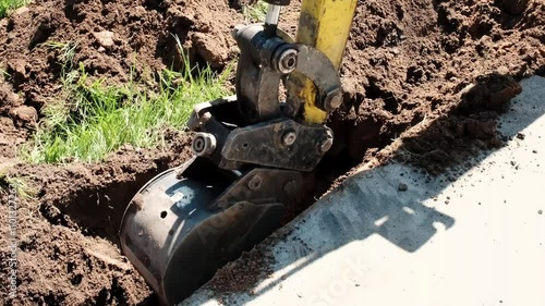 Mini excavator digs a narrow trench in soil for laying communications close-up. Mini bucket of crawler machine. Earthworks with heavy special equipment. Digging machinery works at construction site