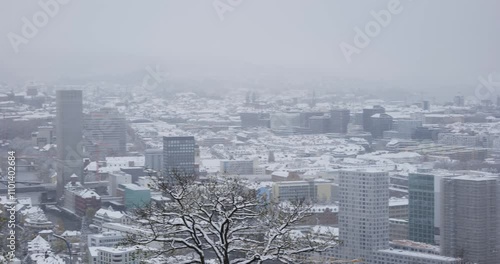 22-11-2024 Zurich, Switzerland. Panning shot of the snow covered city downtown during snowfall. Cloudy weather, snowy rooftops, real time, no people