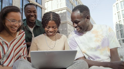 Young students meet up on break for team brainstorm outdoors on campus. Female and male coworkers gather near urban building using laptop. Young man and woman communicate discussing and talking