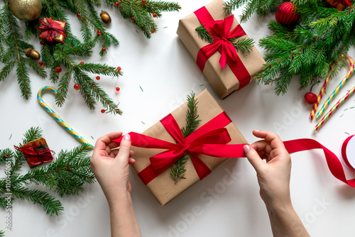 Christmas gift wrapping using eco-friendly materials and pine branches. Tying a gift box with a red ribbon