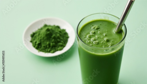 Refreshing bright green spirulina drink sits in a glass equipped with a metal straw. Nearby is a small bowl filled with spirulina powder, set against a soft pastel background