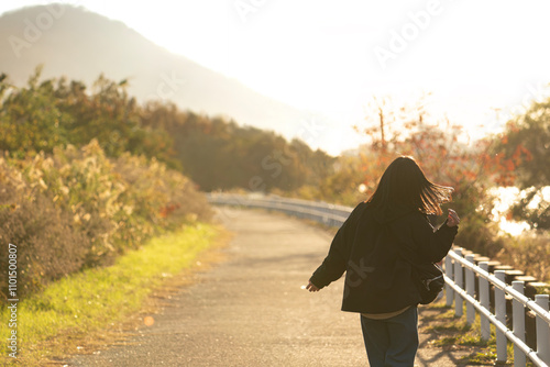 夕方の秋の景色の道を楽しそうに歩く女性の後ろ姿