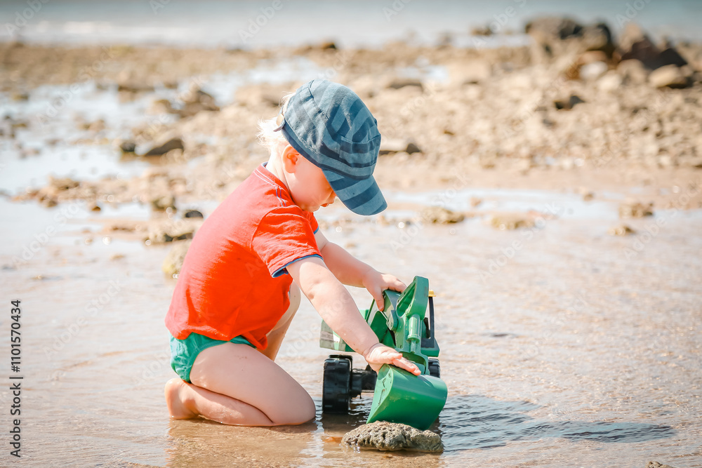 Little boy playing with green digger toy on the beach Little boy playing with green digger toy on the beach