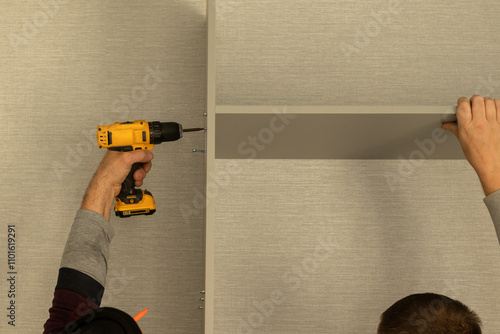 Two men using electronic drill install cabinet