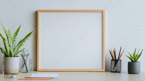 A minimalist workspace featuring a blank frame, potted plants, and art supplies. Perfect for showcasing your work or design.