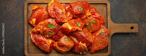 Foto Raw uncooked chopped pieces of pork marinated with seasonings and parsley on wooden cutting board top view on dark rustic background