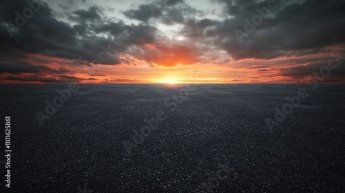 Dramatic sunset illuminating a textured dark asphalt landscape under a sky filled with dynamic clouds and vibrant hues of orange and red. photo