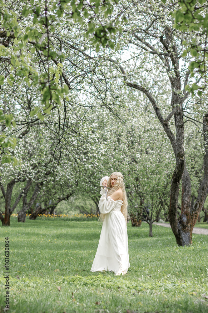 Romantic young blonde in white dress with sword among white blossoming apple trees in garden. Warrior woman Romantic young blonde in white dress with sword among white blossoming apple trees in garden. Warrior woman