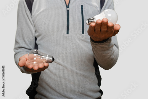 Man doing comparison between various types of LED and incandescent light bulb, Light bulb replacement: man holding incandescent and LED bulbs, highlighting power consumption and utility bill impact