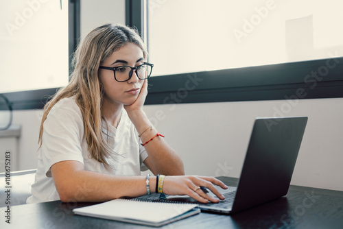 Portrait of serious millennial caucasian female student sit at desk at home study online on laptop. Thoughtful young attractive woman use computer take distant course or training. Education concept..